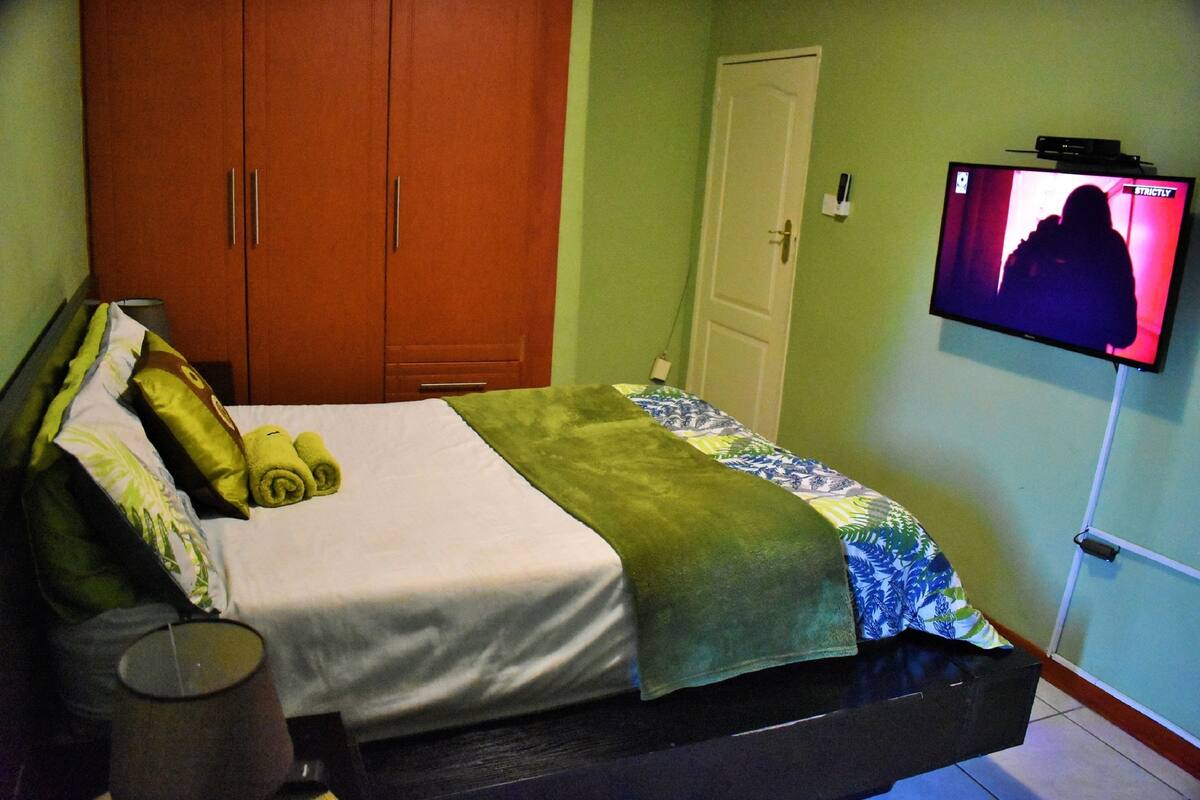 A hotel room with a bed, a wardrobe, a television on the wall, and a bedside table with a lamp.