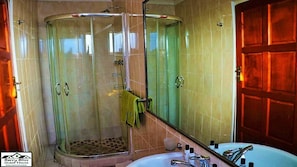 A bathroom with a glass shower enclosure, a sink with a mirror, and wooden doors. - Berry Bliss Guest House (Gaborone)