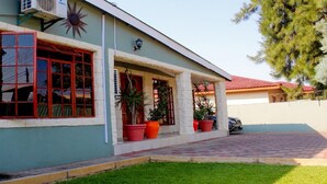 A two-story house with a green exterior, red-framed windows, and a tiled driveway. - Berry Bliss Guest House (Gaborone)