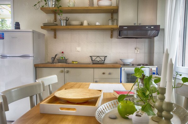 A kitchen with wooden shelves, a built-in oven, and a dining table with chairs. - Kopana Resort (Kassandra)