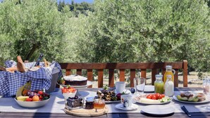 A picnic table set with various foods and drinks, surrounded by olive trees and a view of the sea. - Kopana Resort (Kassandra)