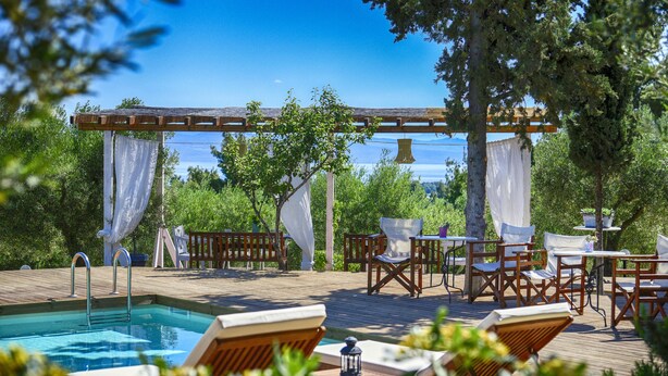 A poolside area with wooden deck, lounge chairs, and a pergola with white curtains. - Kopana Resort (Kassandra)