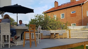 An outdoor patio with wicker furniture, a table, and a wooden deck. - Gävle Pendlarlägenhet (Gävle)