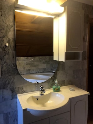 A bathroom with a marble wall, a white sink, a mirror, and a soap dispenser. - Gävle Pendlarlägenhet (Gävle)