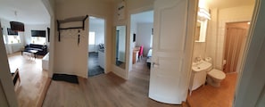 A spacious living area with a sofa, coffee table, and a hanging light fixture. There is a hallway leading to a bathroom with a sink and toilet. - Gävle Pendlarlägenhet (Gävle)