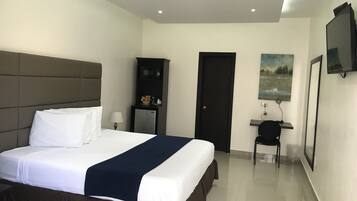 Habitación de hotel con una cama grande, un escritorio, una silla, un televisor y una puerta.