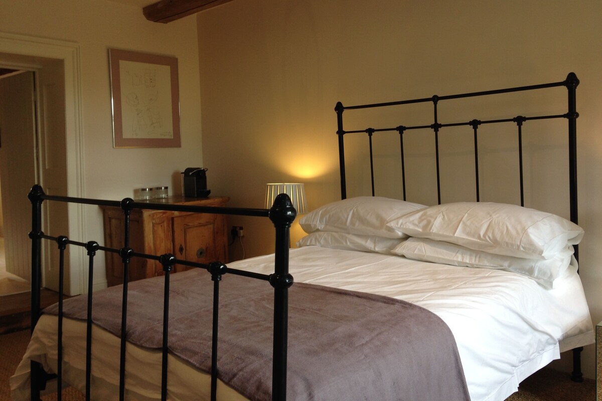 A bed with a metal frame, a wooden dresser, and a framed picture on the wall.