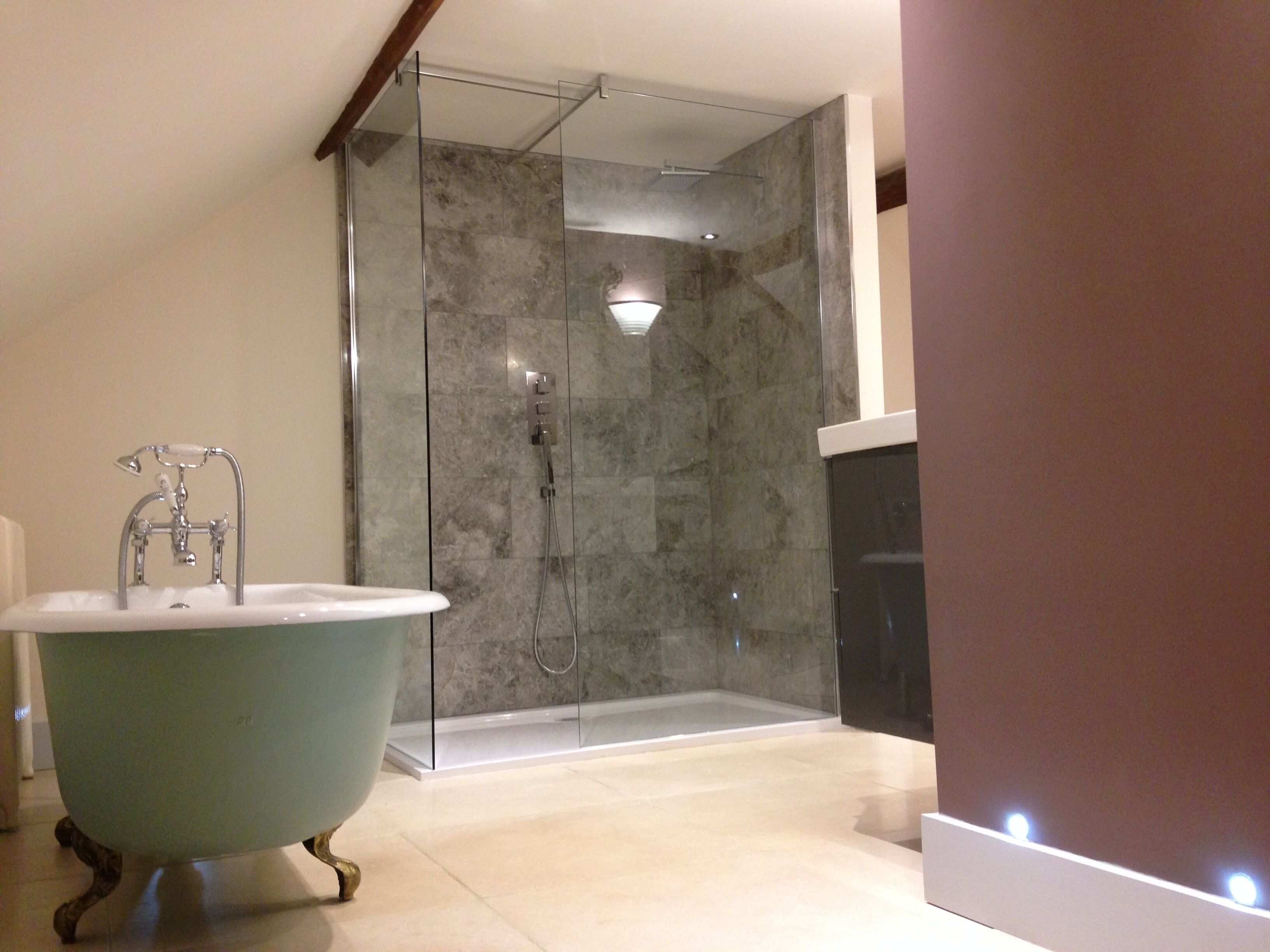 Un baño moderno con una bañera independiente, ducha con mampara de vidrio y pared revestida de mármol.