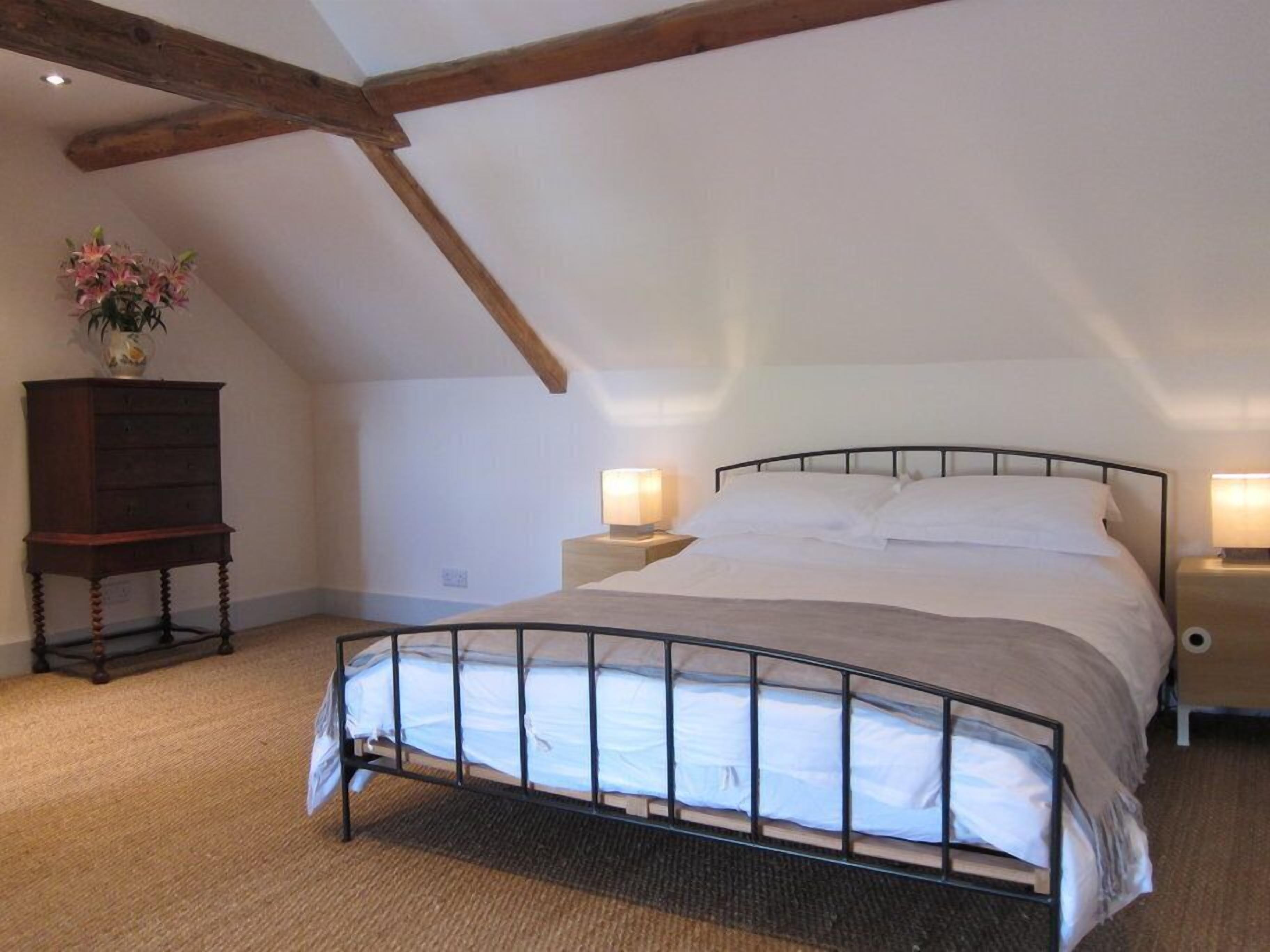 Una cama individual con estructura metálica, un aparador de madera y dos lámparas de noche en una habitación con techos inclinados.