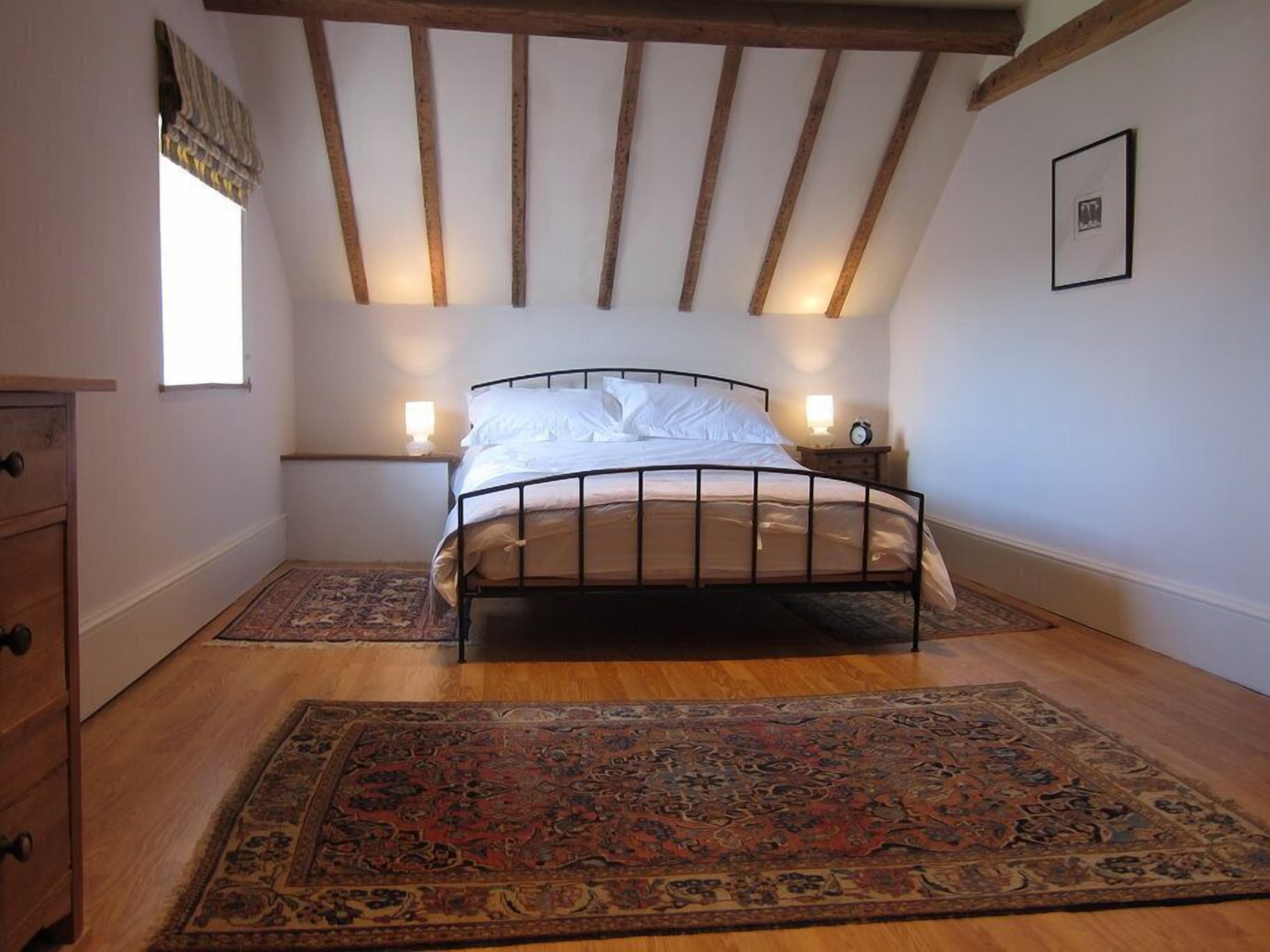 Une chambre à coucher comprenant un lit, deux tables de chevet, une petite table, une commode en bois et un grand tapis à motifs.