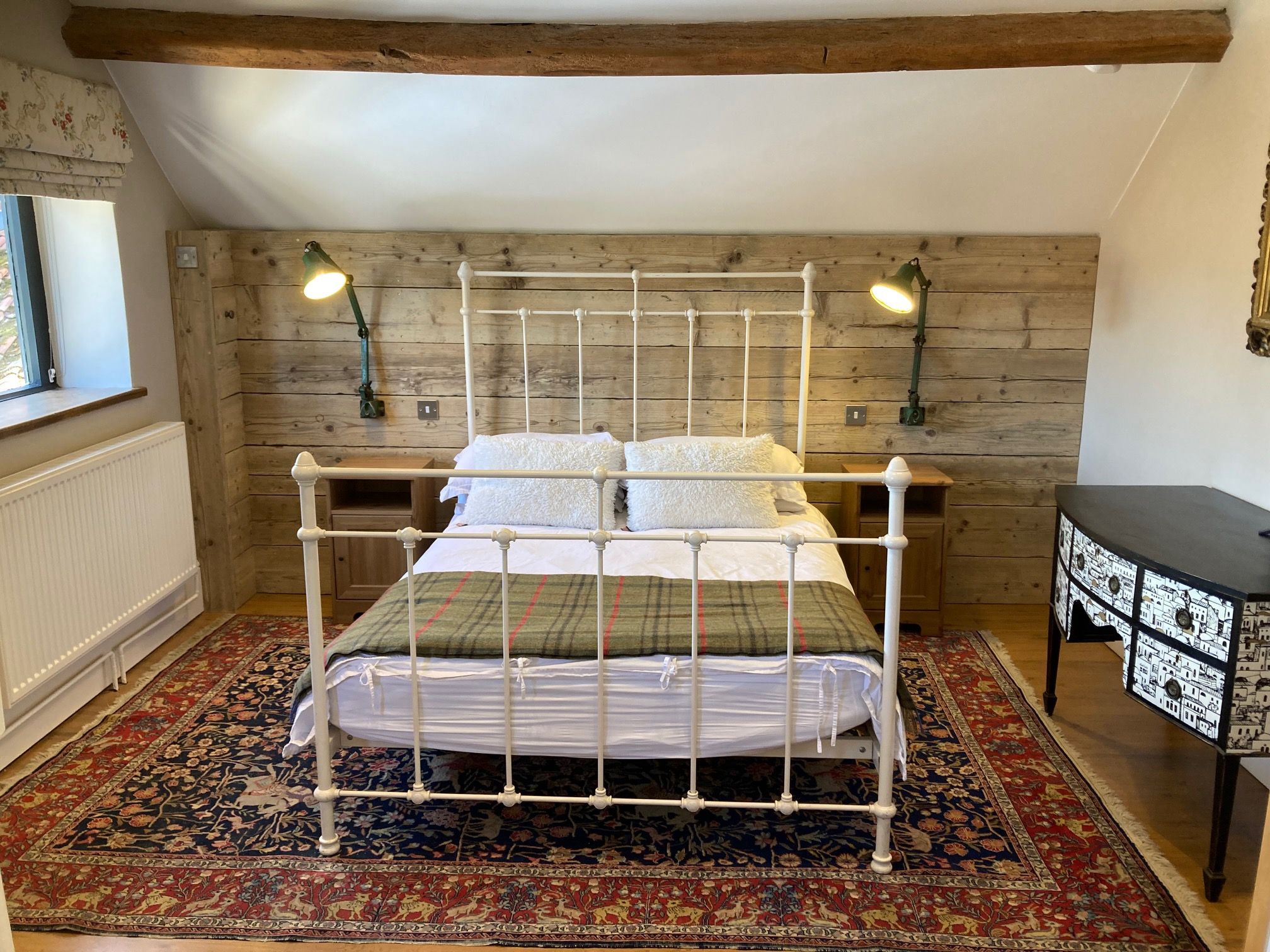 Ein Schlafzimmer mit Himmelbett, zwei Nachttischlampen, einer Heizung, einem gemusterten Teppich und einem Nachttisch mit dekorativer Lampe.