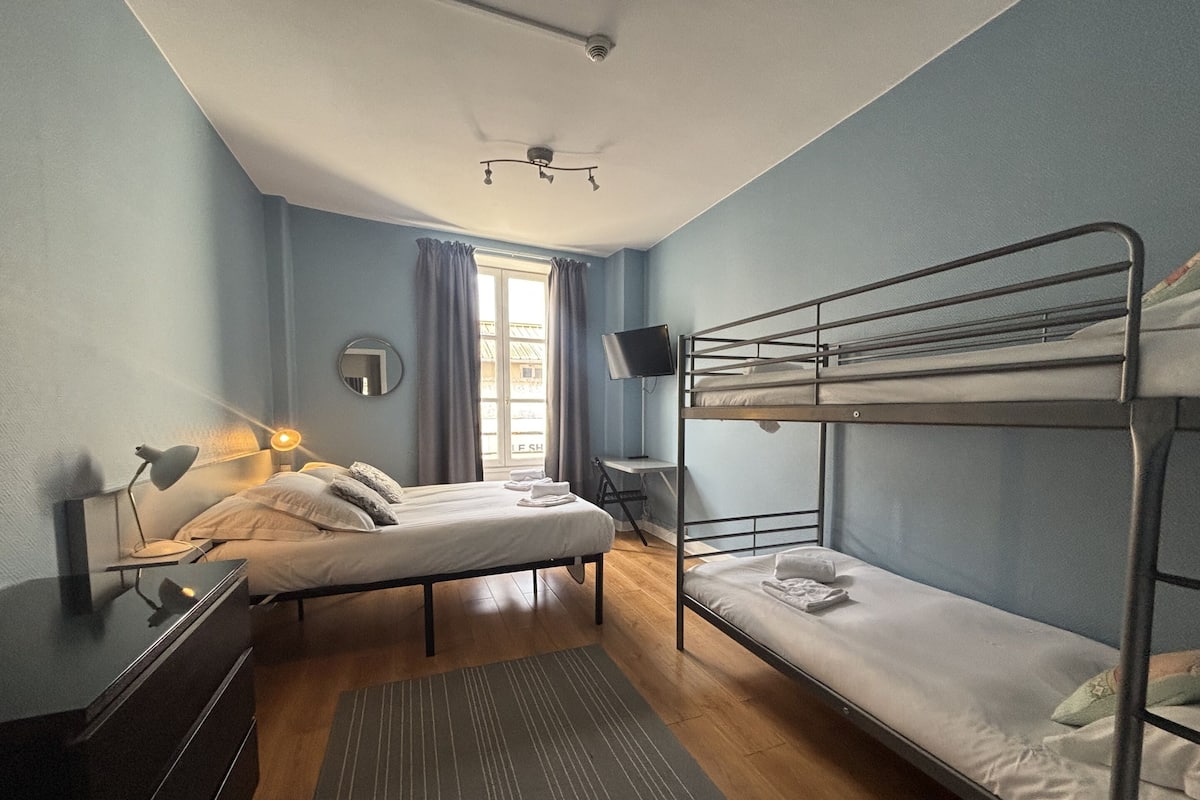 Une chambre avec des lits superposés, un bureau, une chaise, une télévision et une fenêtre avec des rideaux.