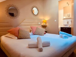 Habitación de hotel con cama, almohadas, mesita de noche con lámpara, espejo y baño visible a través de una puerta abierta.