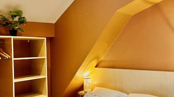A bedroom with a bed, pillows, a bedside table with a lamp, a hanging plant, and a built-in wardrobe.
