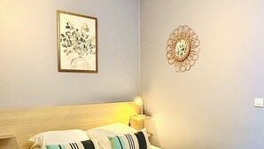 Ein ordentlich bezogenes Bett mit Kissen und Handtüchern, eine Nachttischlampe und ein gerahmtes Pflanzenbild an der Wand.