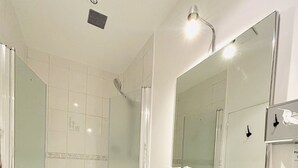 Ein modernes Badezimmer mit einer gläsernen Duschkabine, einem weißen Waschbecken und einem Spiegel darüber.