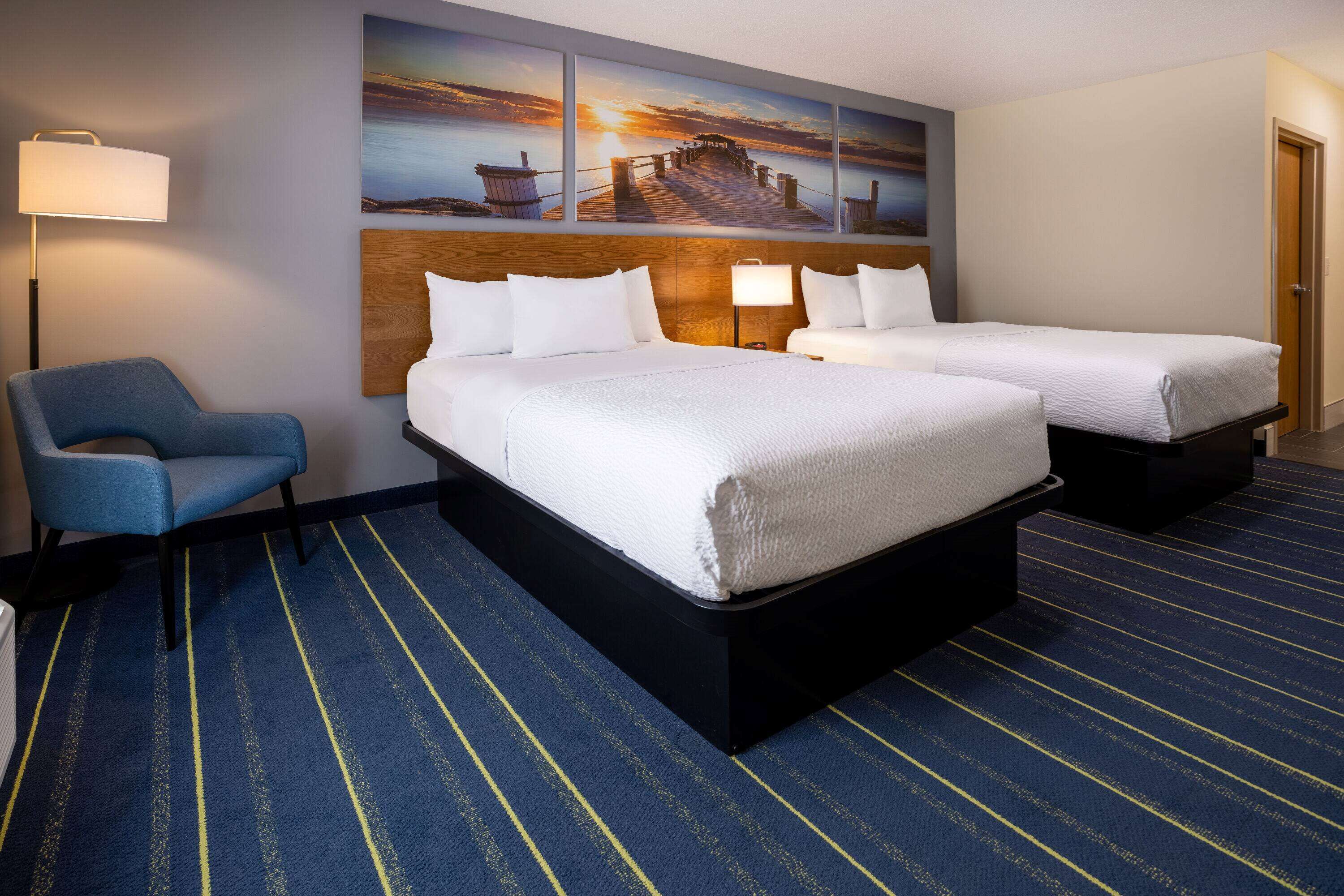 A hotel room with two beds, a blue chair, and a large wall painting.