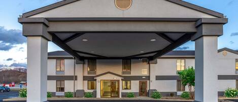 A modern hotel entrance with a covered walkway, large windows, and a landscaped front yard.