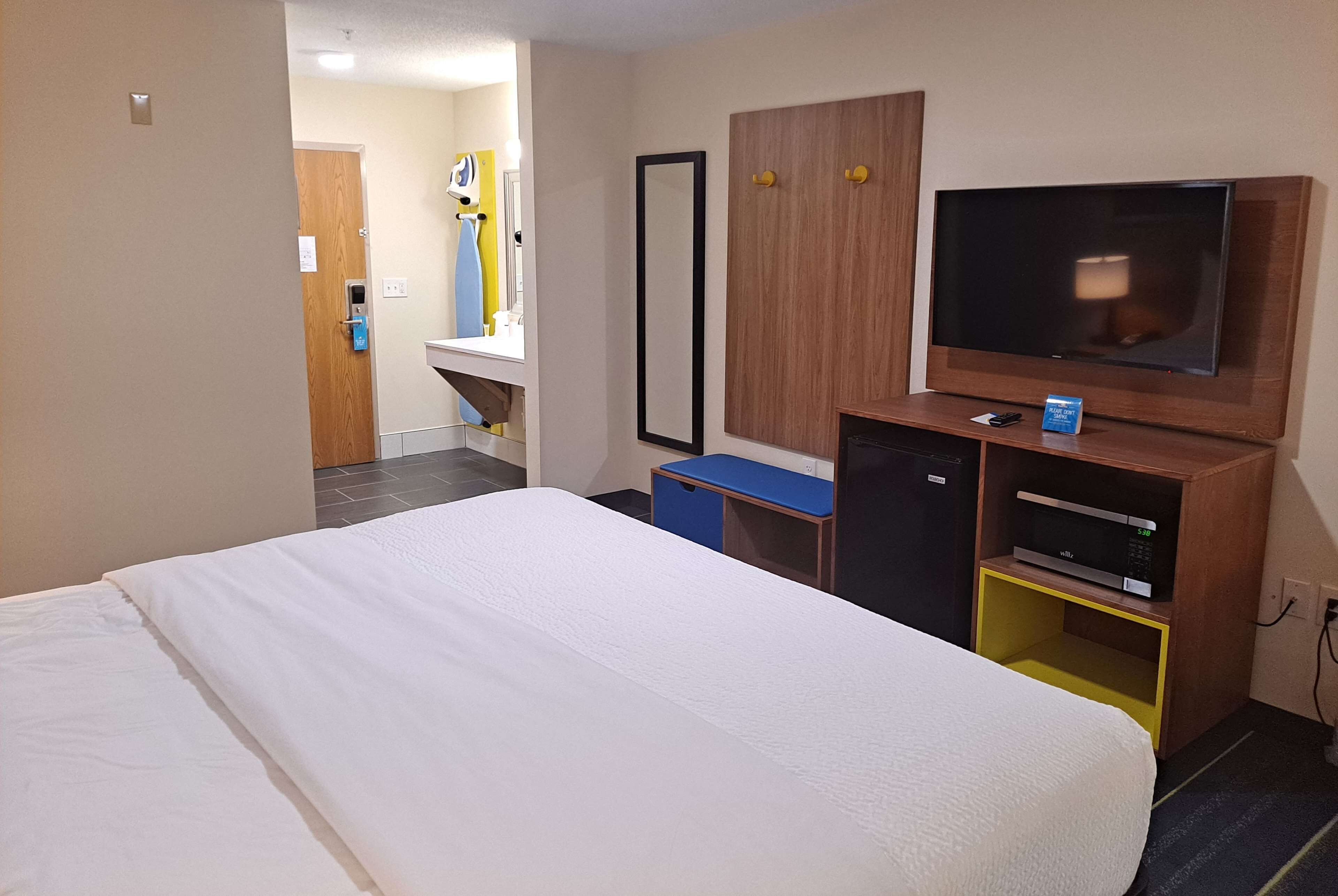Et hotelværelse med en stor seng, fjernsyn, mikroovn og et lille skrivebord.