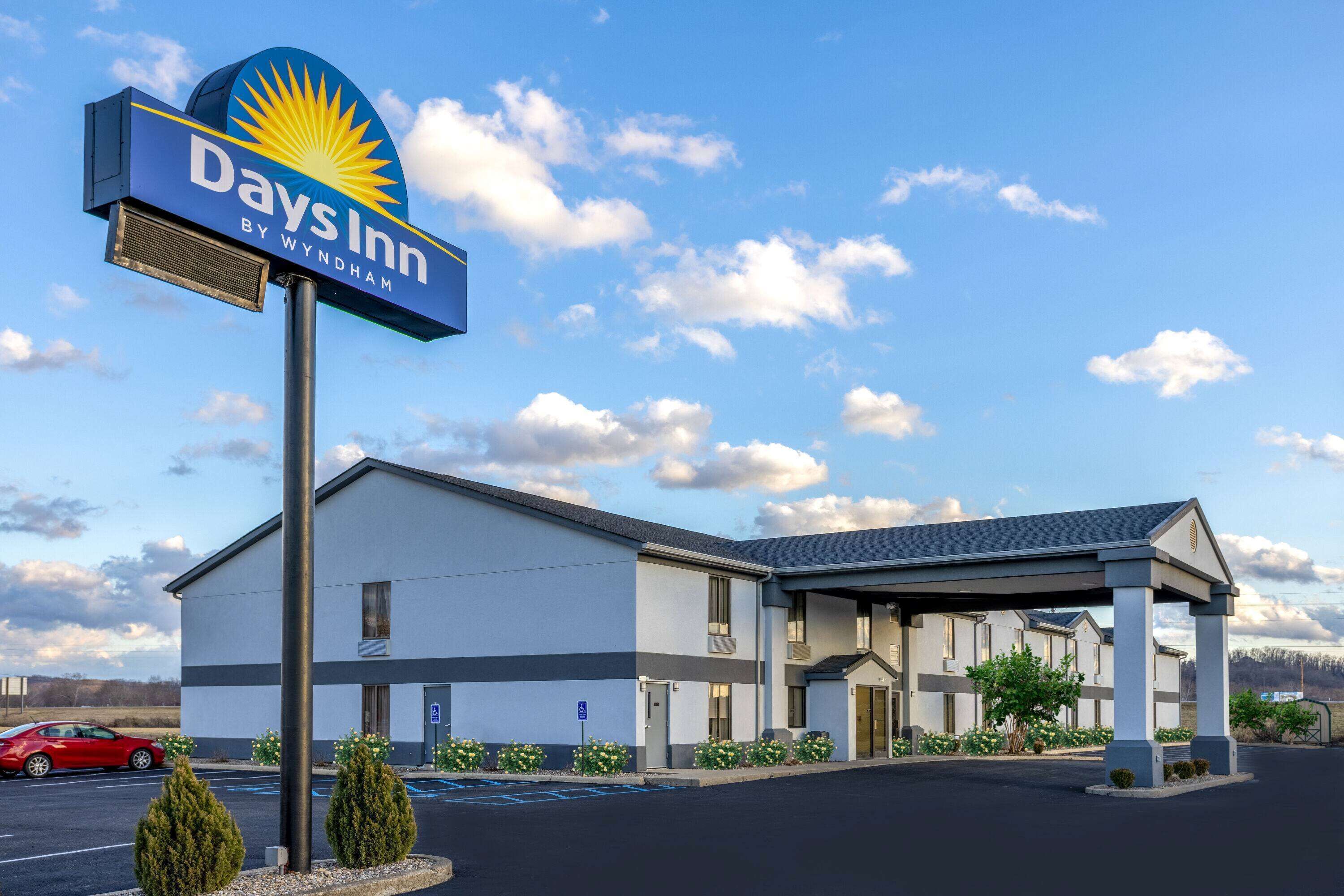 A Days Inn by Wyndham hotel with a parking lot, a covered entrance, and a clear sky.
