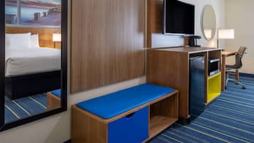 Una camera d'albergo con un letto, una scrivania con un computer, una televisione, uno specchio e un piccolo angolo salotto.