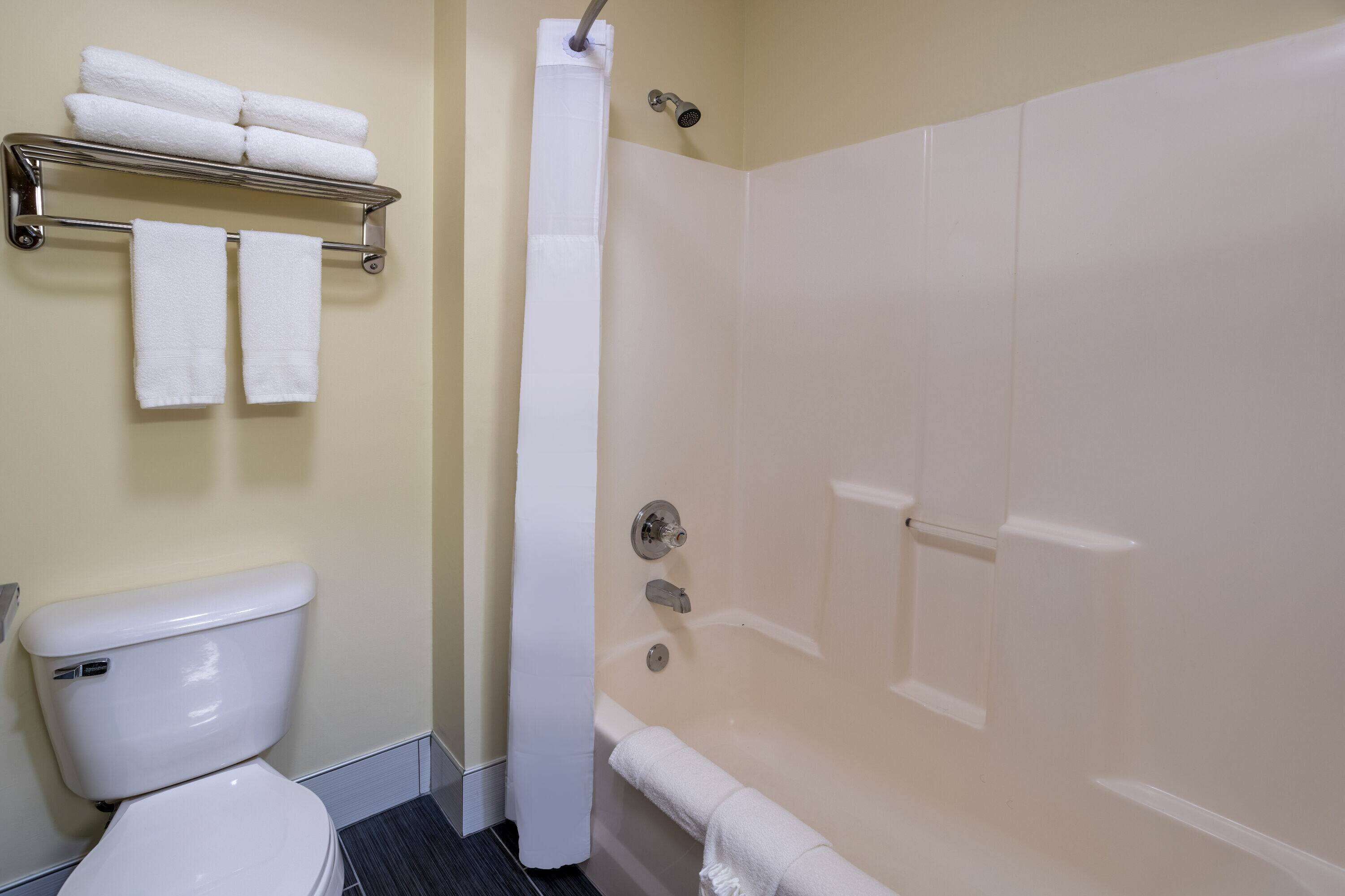 A bathroom with a toilet, a shower with a glass door, and a towel rack with folded towels.