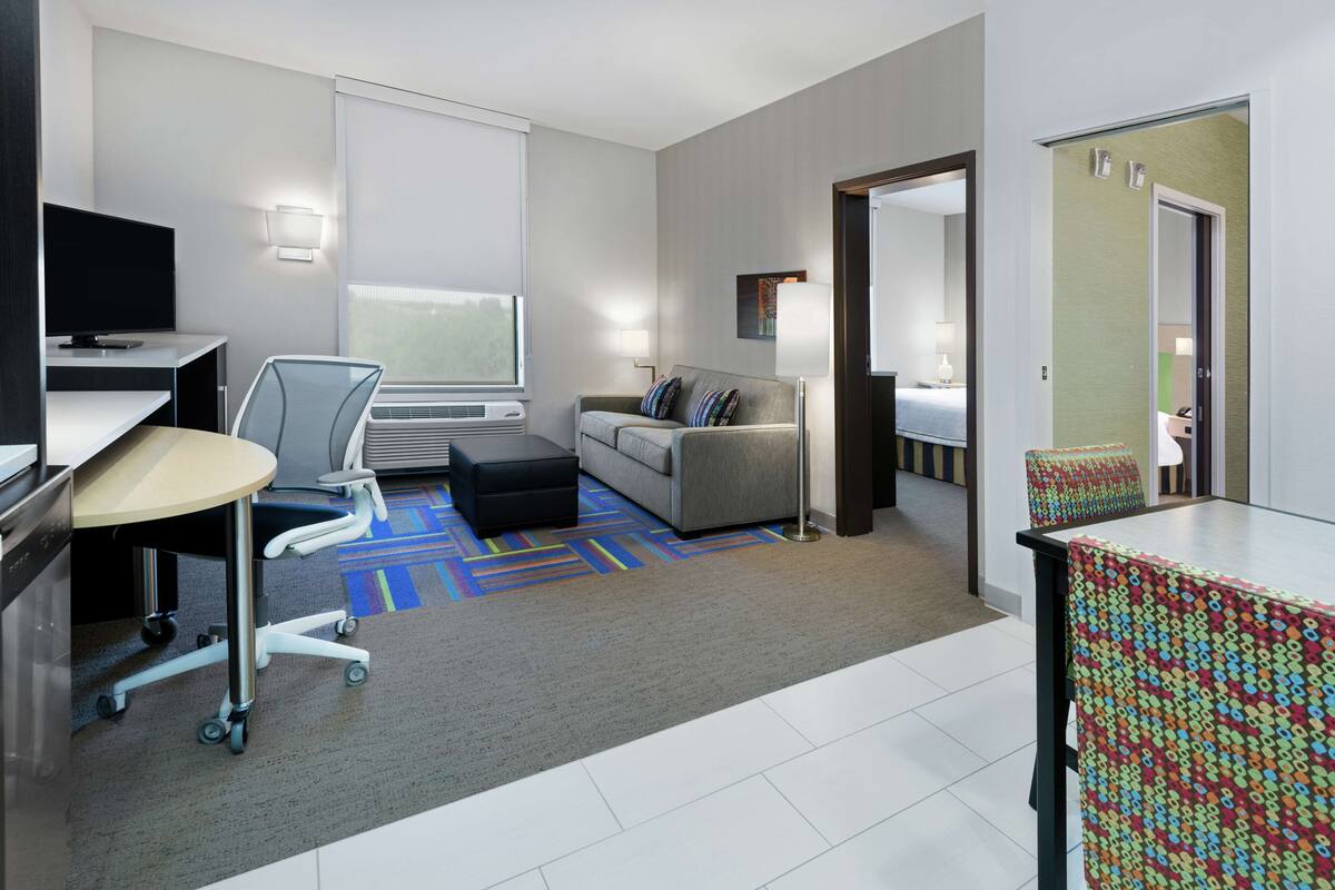 A modern hotel room with a desk, chair, sofa, and a colorful rug.