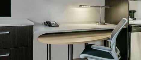 A modern office desk with a telephone, a desk lamp, and a chair with wheels.