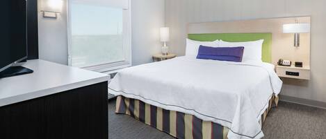 A hotel room with a bed, bedside tables, a TV, and a window.