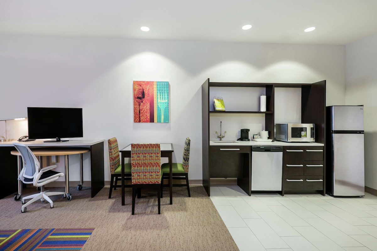 A modern kitchen with a microwave, refrigerator, and a dining area with chairs and a table.