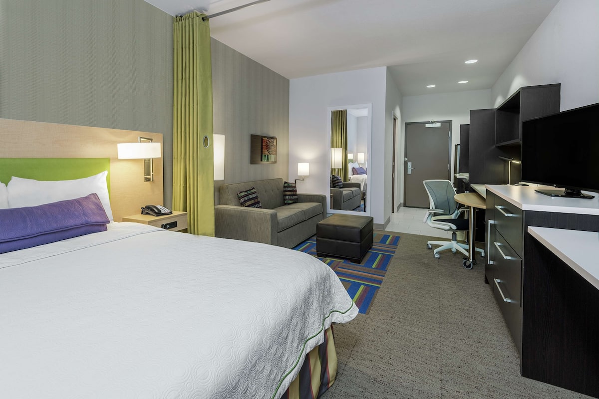 A hotel room with a large bed, a desk with a television, a sofa, and a small table.