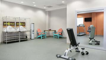 A gym with exercise equipment, a mirror, and two chairs.