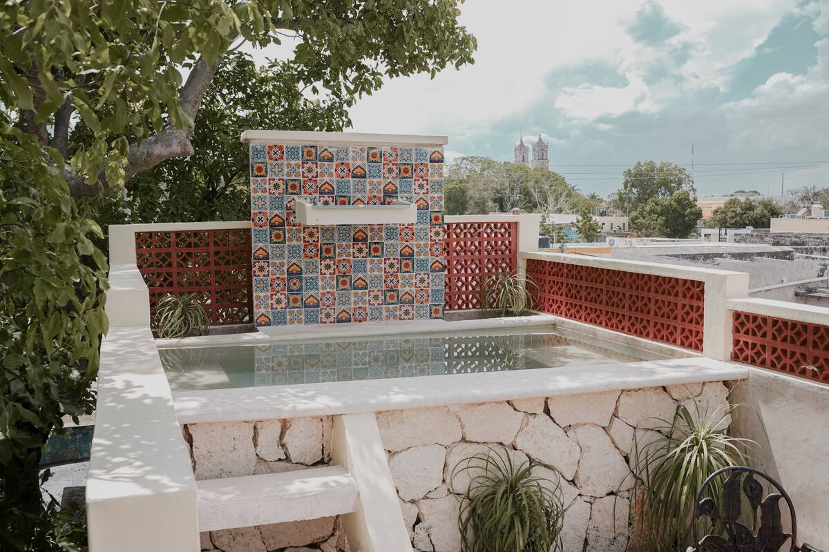 Une piscine sur le toit, avec un mur carrelé et des marches en pierre, entourée de verdure et avec une vue sur la ville en arrière-plan.