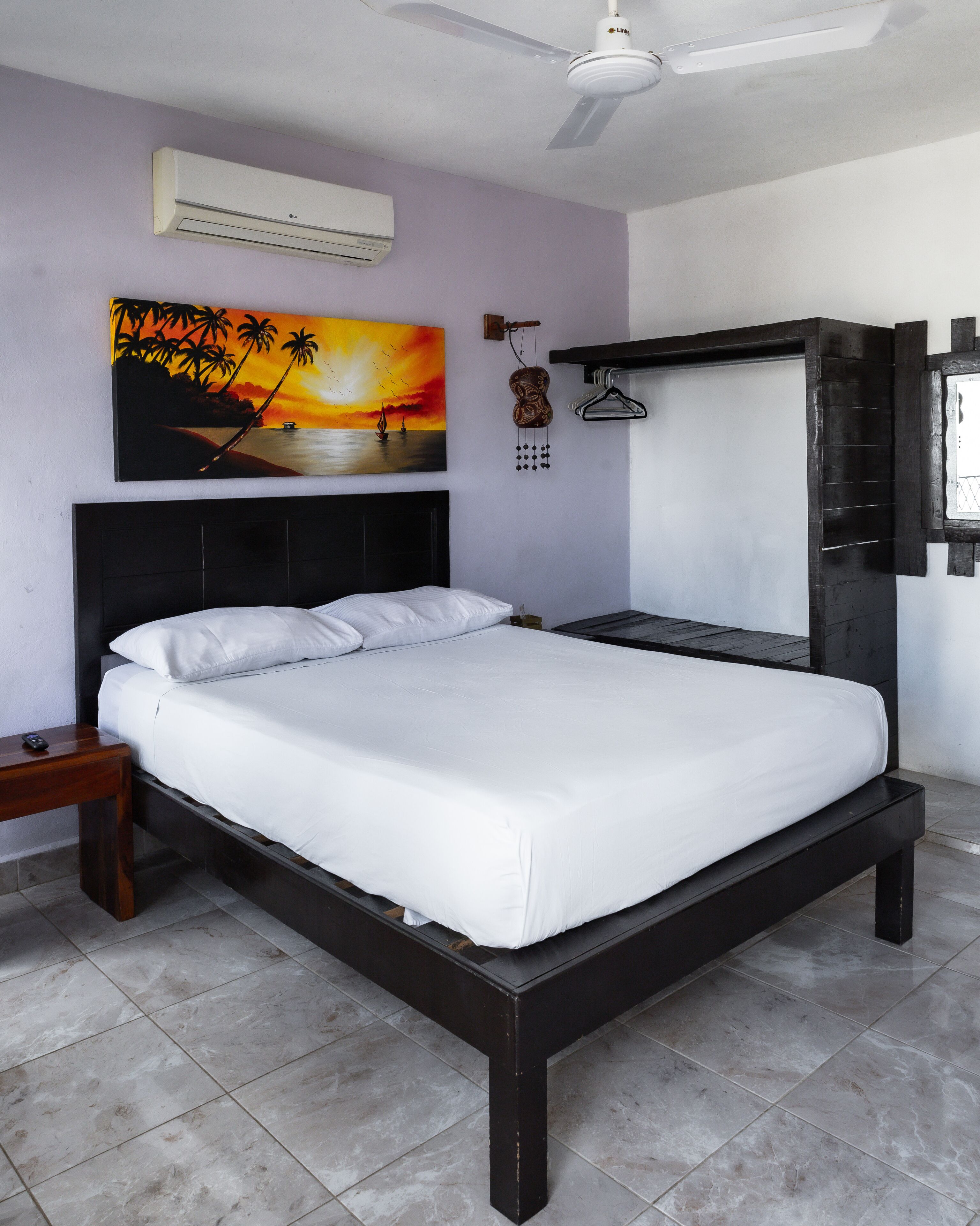 Un dormitorio con cama, mesita de noche, aire acondicionado instalado en la pared, un cuadro, una guitarra de madera y un perchero.