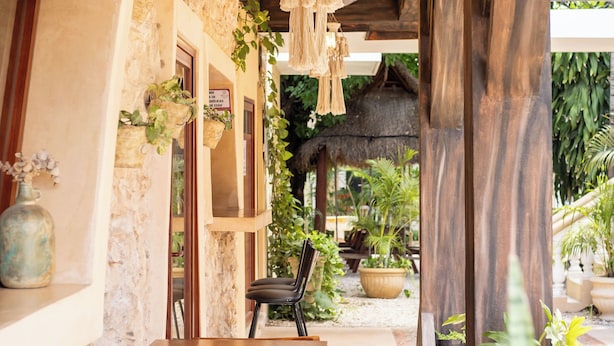 A covered outdoor seating area with wooden tables and chairs, surrounded by stone walls and potted plants. - Hotel Tunich Naj (Valladolid)