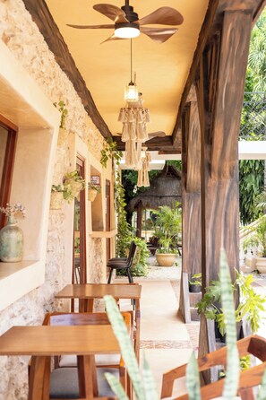 A covered outdoor seating area with wooden tables and chairs, surrounded by stone walls and potted plants. - Hotel Tunich Naj (Valladolid)