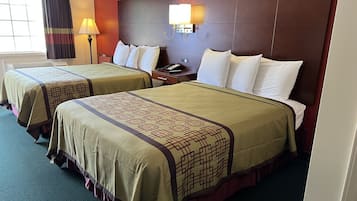 A hotel room with two beds, each with a patterned bedspread, a headboard with a light fixture, and a window with curtains.
