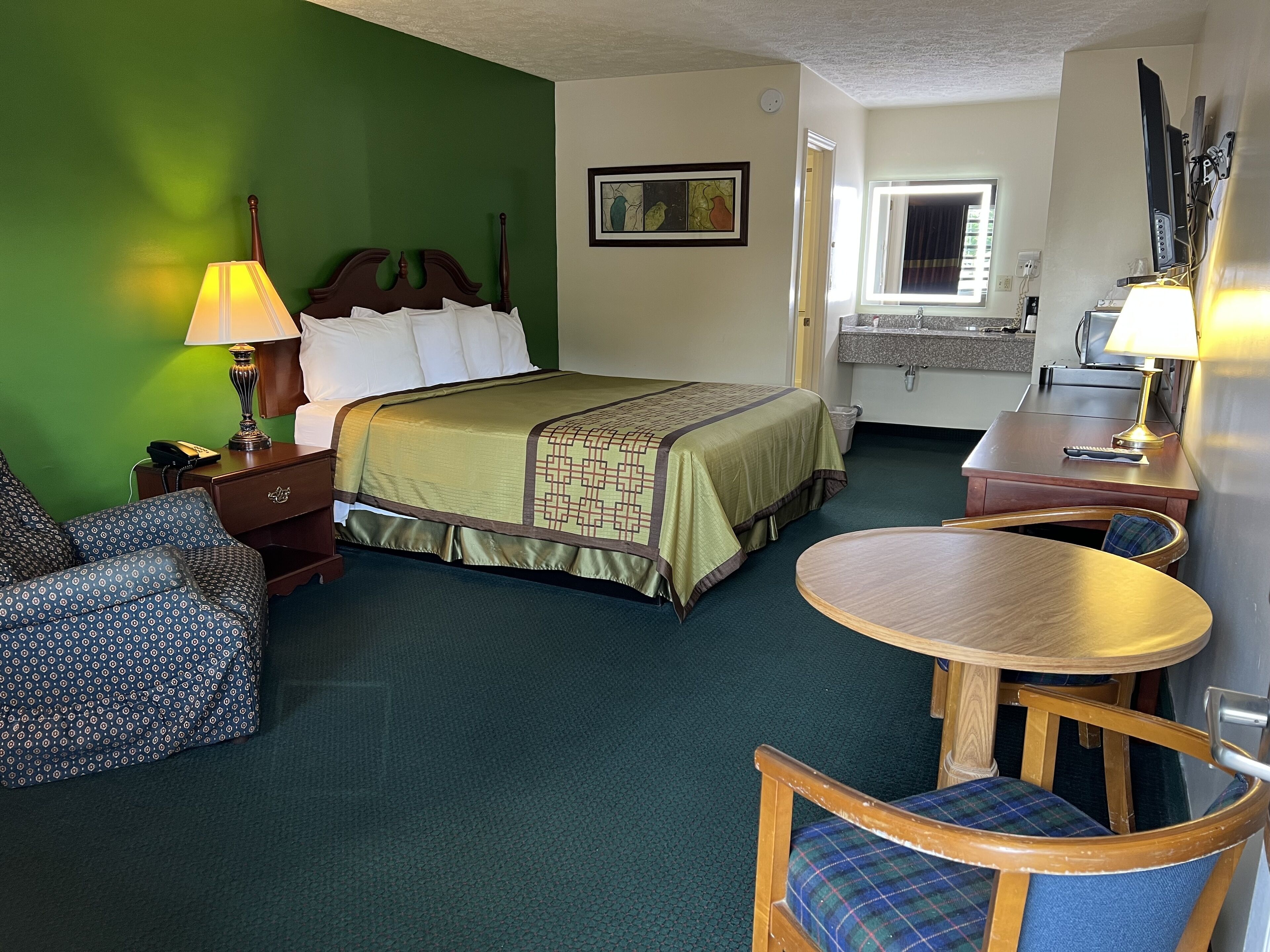 Una habitación de hotel con una cama, un escritorio, una silla, una lámpara y un cuadro en la pared.