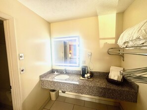 A compact bathroom with a granite countertop, a sink, a mirror, a hairdryer, and a towel rack.