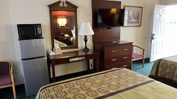 A hotel room with a bed, a desk with a lamp, a television, a microwave, and a refrigerator.