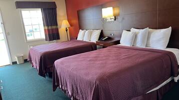 Habitación de hotel con dos camas, una mesita de noche, una lámpara y una ventana con cortinas.