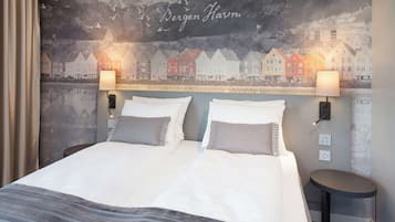 A double bed with two pillows, a bedside table, and a wall mural of houses.