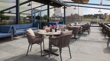 An outdoor patio with seating and tables, large windows offering views of the surrounding area.