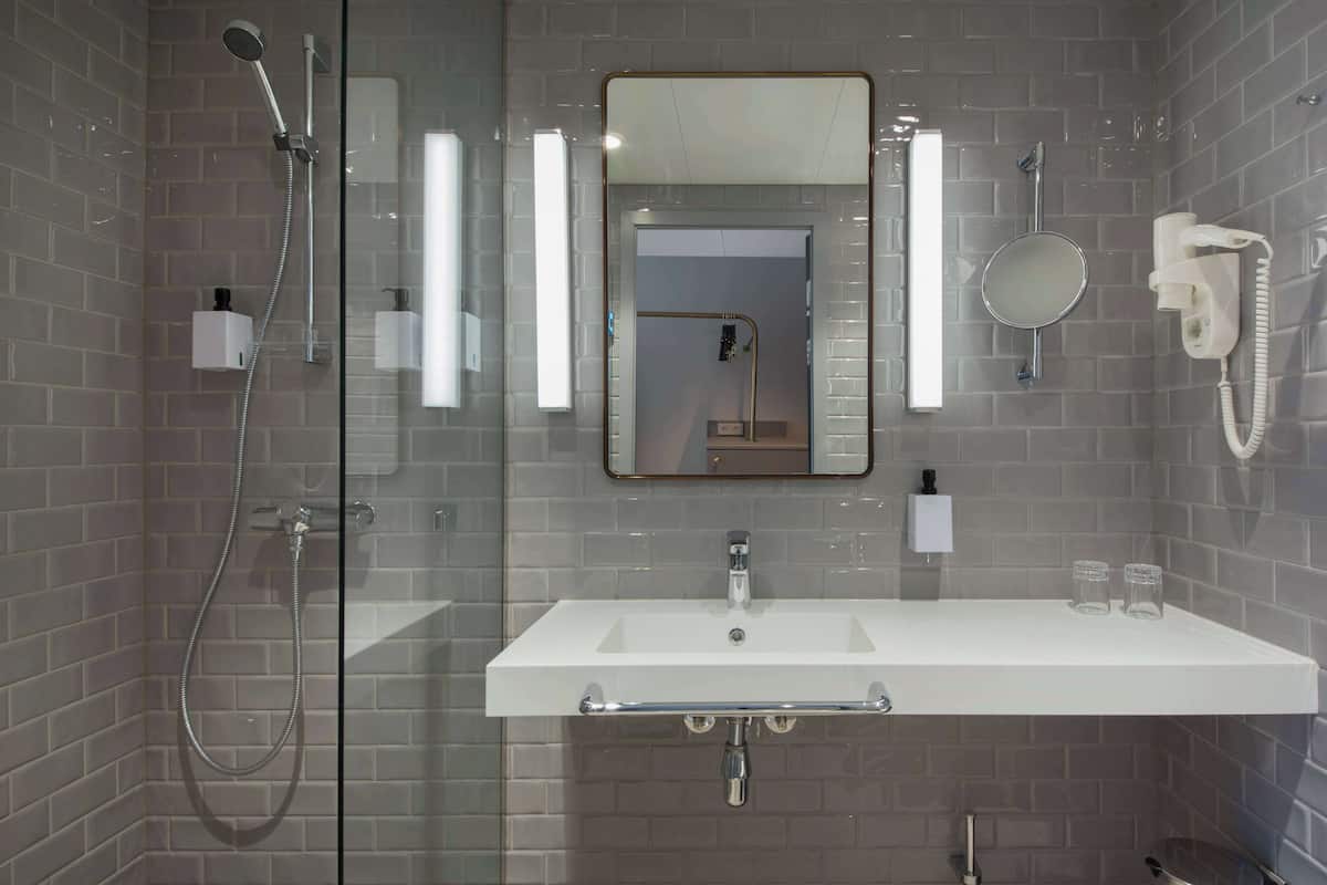 A modern bathroom with a glass-enclosed shower, a white sink with a mirror above it, and a hairdryer on the wall.