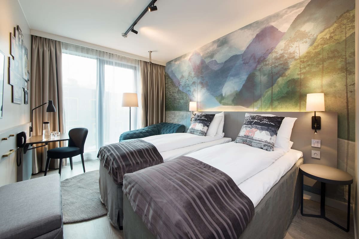 A hotel room with two beds, a desk, a chair, and a large wall mural.