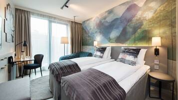 A hotel room with two beds, a desk, a chair, and a large wall mural.