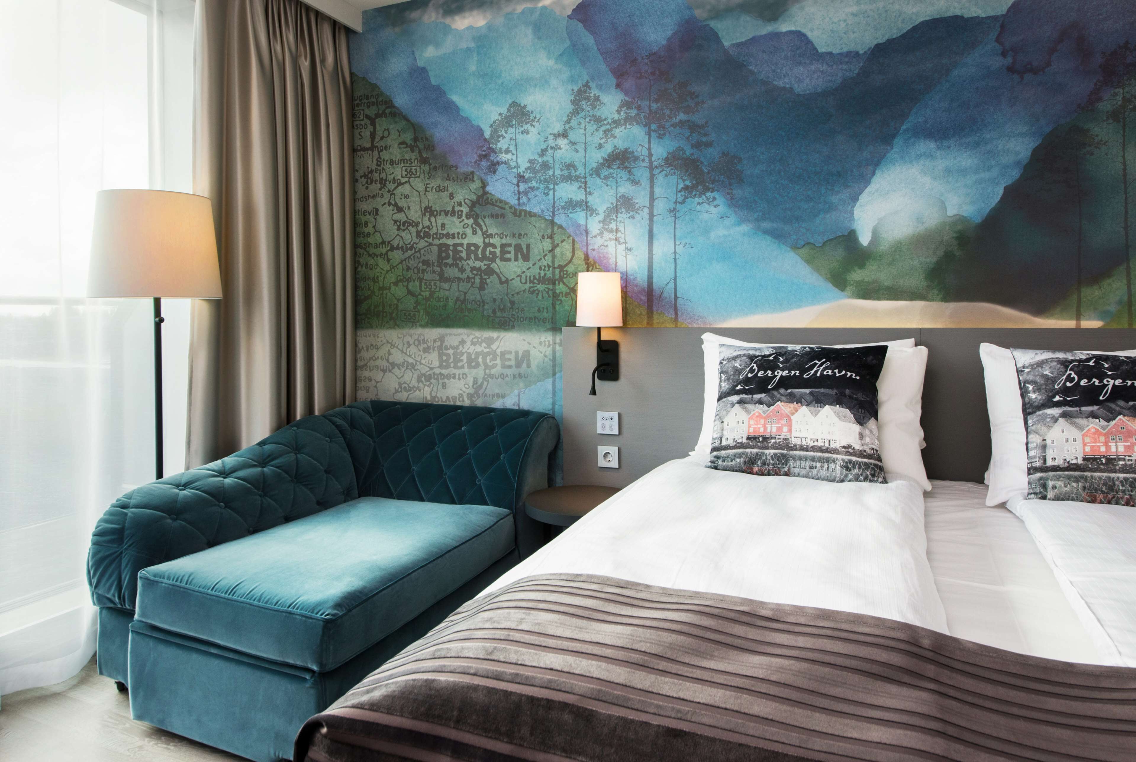 A hotel room with a large bed, a blue sofa, a map mural on the wall, and a lamp.