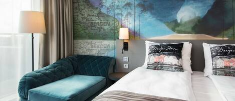 A hotel room with a large bed, a blue sofa, a map mural on the wall, and a lamp.