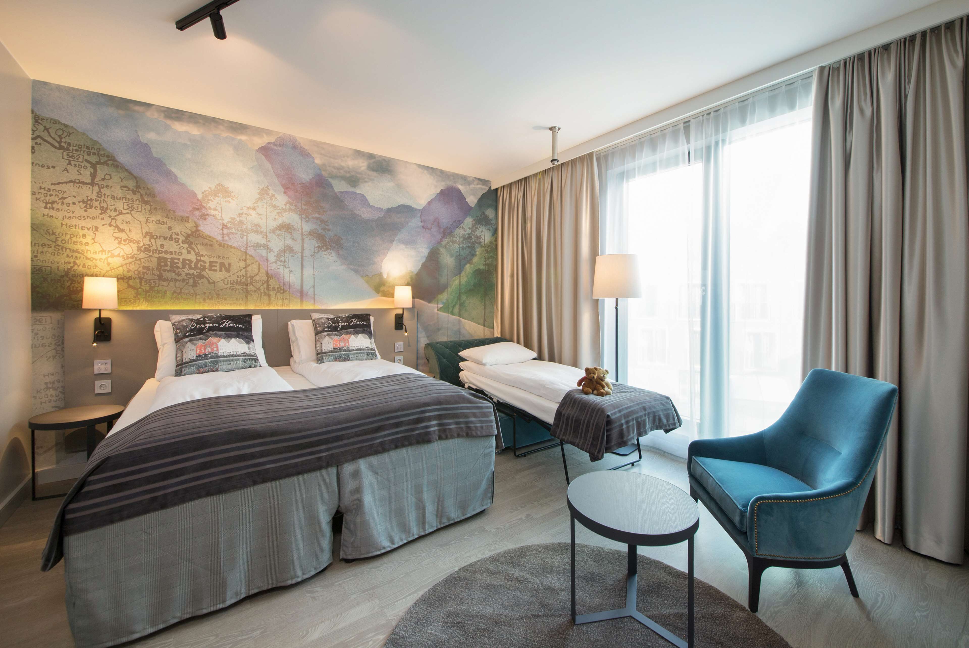 Habitación de hotel con dos camas, un escritorio, una silla, un mapa en la pared y un ventanal con cortinas.