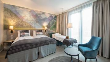 Habitación de hotel con dos camas, un escritorio, una silla, un mapa en la pared y un ventanal con cortinas.